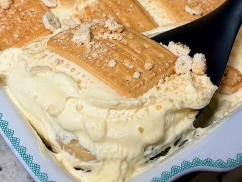 A white baking dish filled with creamy banana pudding and layered golden biscuits, topped with crushed biscuit crumbs.