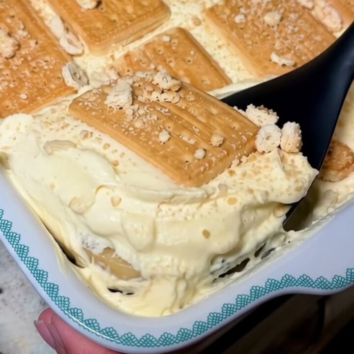 A white baking dish filled with creamy banana pudding and layered golden biscuits, topped with crushed biscuit crumbs.