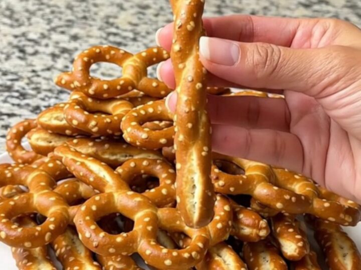 A plate of green witch finger pretzel rods with almond nails, arranged on a dark baking sheet.
