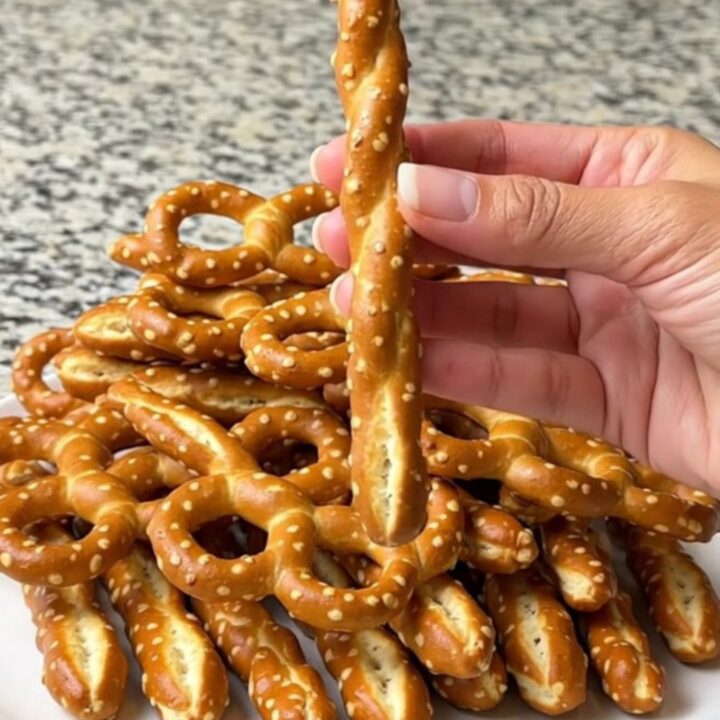 A plate of green witch finger pretzel rods with almond nails, arranged on a dark baking sheet.