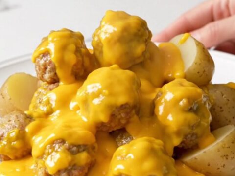 A top-down view of the slow cooker filled with turkey meatballs and halved baby potatoes covered in a creamy cheddar sauce.