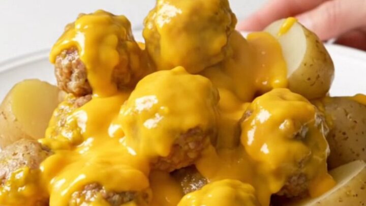 A top-down view of the slow cooker filled with turkey meatballs and halved baby potatoes covered in a creamy cheddar sauce.