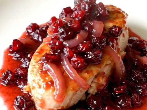 A top-down view of raw chicken breasts being arranged in a black slow cooker with onions and seasonings.