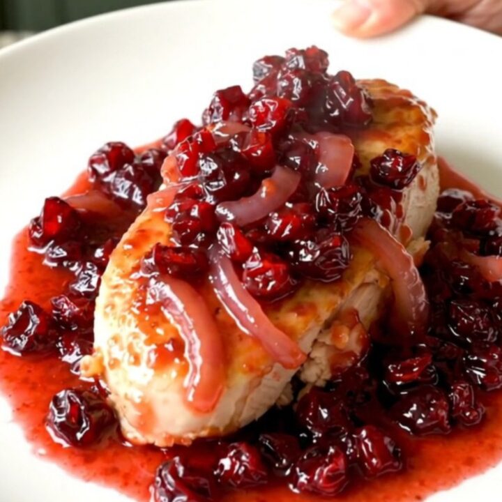 A top-down view of raw chicken breasts being arranged in a black slow cooker with onions and seasonings.