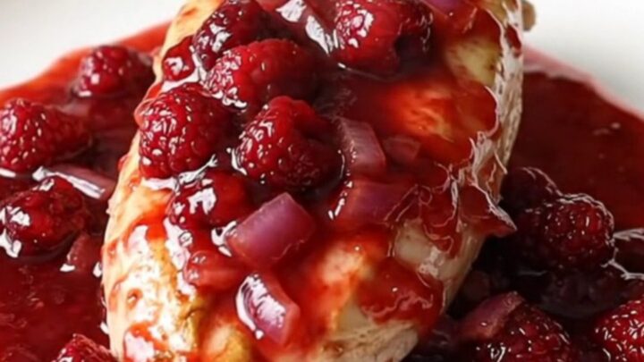 A plate featuring soft-braised chicken breasts covered in a glossy, red raspberry and onion sauce.