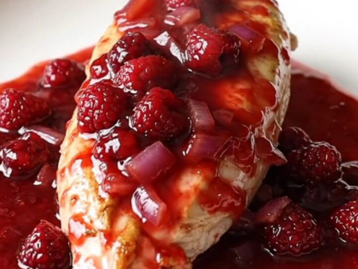 A plate featuring soft-braised chicken breasts covered in a glossy, red raspberry and onion sauce.
