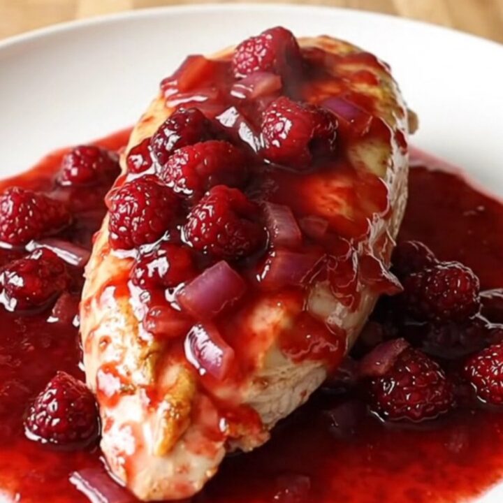 A plate featuring soft-braised chicken breasts covered in a glossy, red raspberry and onion sauce.