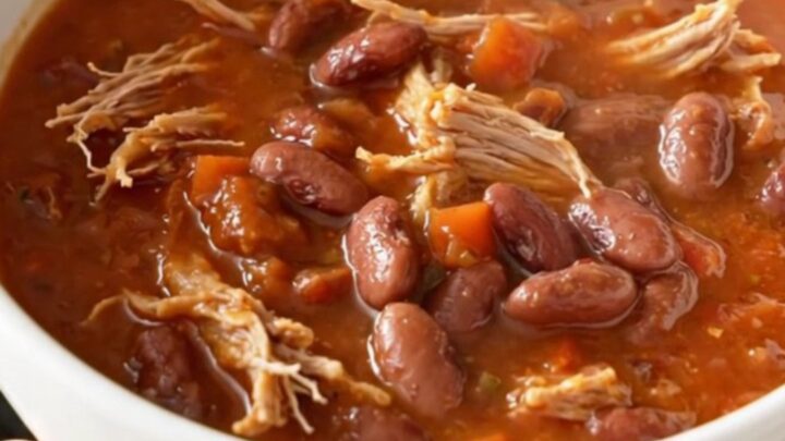 A hearty bowl of slow cooker pulled pork chili with pinto beans, garnished with fresh herbs.