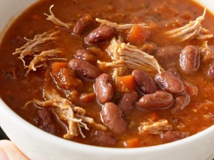A hearty bowl of slow cooker pulled pork chili with pinto beans, garnished with fresh herbs.