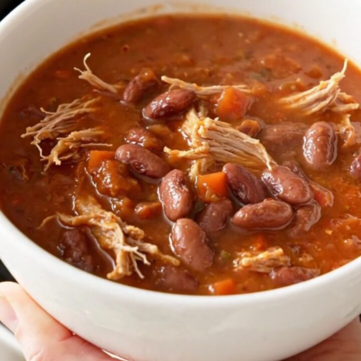 A hearty bowl of slow cooker pulled pork chili with pinto beans, garnished with fresh herbs.