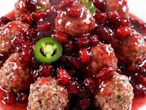 A close-up of a slow cooker filled with turkey meatballs coated in a glossy, dark red cranberry and jalapeno sauce.