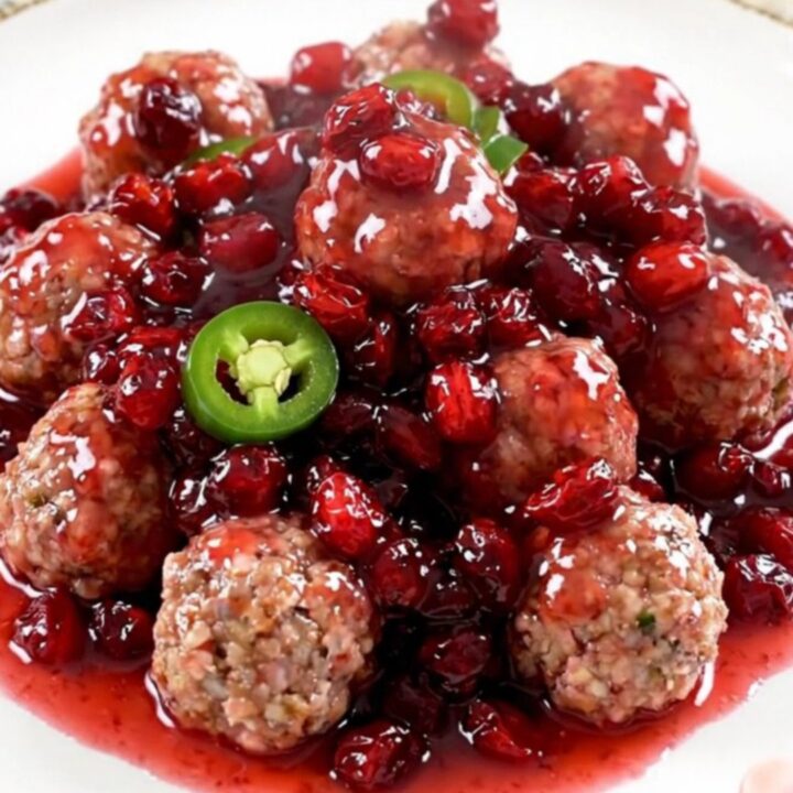 A close-up of a slow cooker filled with turkey meatballs coated in a glossy, dark red cranberry and jalapeno sauce.