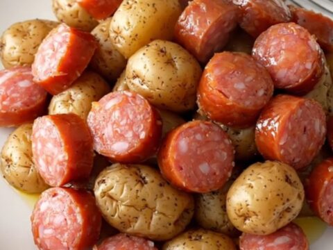 A close-up of a slow cooker filled with golden baby potatoes and sliced smoked sausage