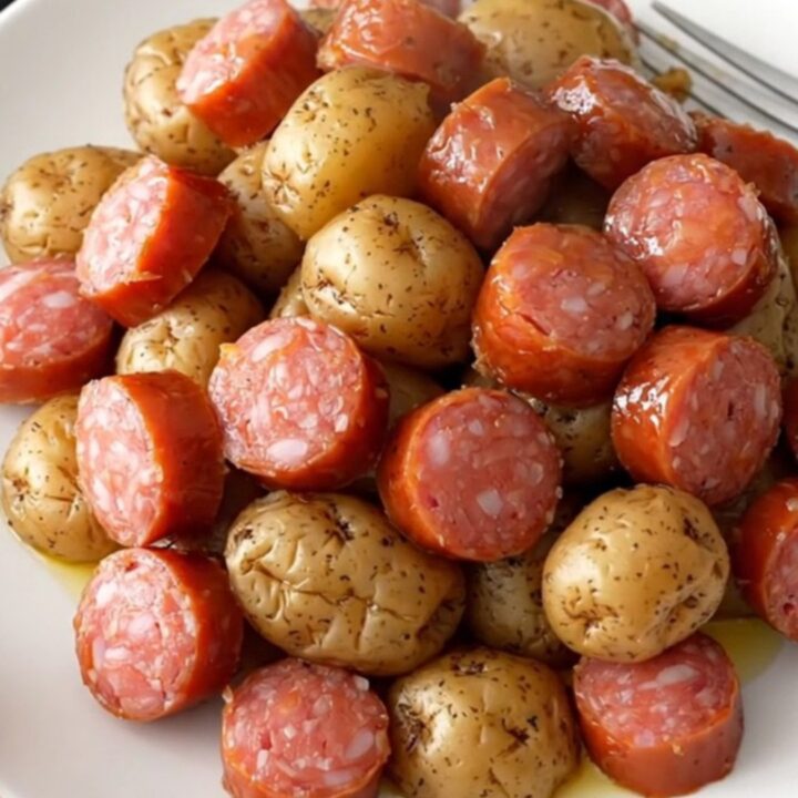 A close-up of a slow cooker filled with golden baby potatoes and sliced smoked sausage