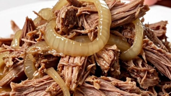 A close-up of tender, shredded pulled pork with caramelized onions in a slow cooker, showing juicy textures.