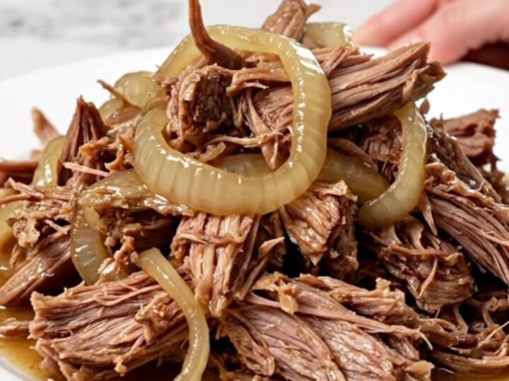 A close-up of tender, shredded pulled pork with caramelized onions in a slow cooker, showing juicy textures.