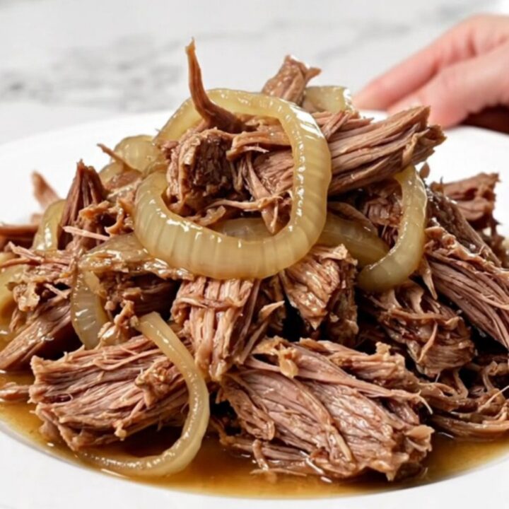A close-up of tender, shredded pulled pork with caramelized onions in a slow cooker, showing juicy textures.