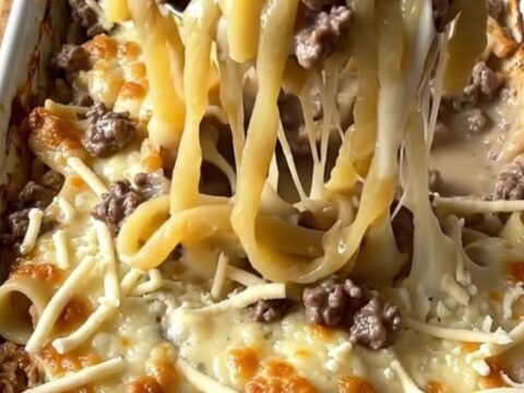 A top-down view of a rectangular baking dish filled with raw noodles, ground beef, and creamy sauce.