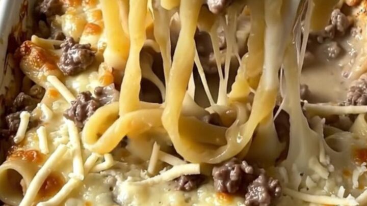 A top-down view of a rectangular baking dish filled with raw noodles, ground beef, and creamy sauce.