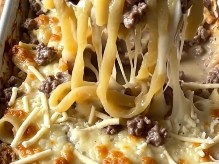 A top-down view of a rectangular baking dish filled with raw noodles, ground beef, and creamy sauce.