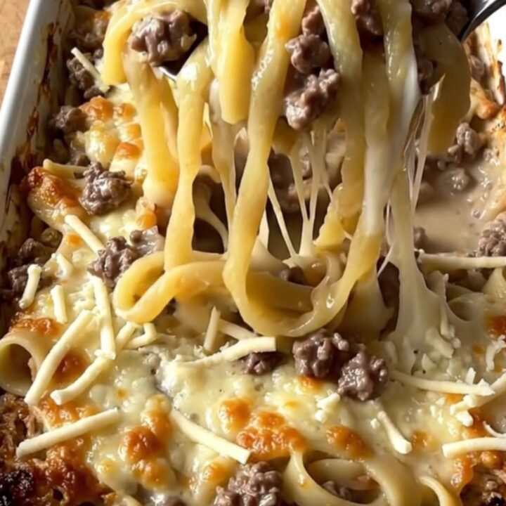 A top-down view of a rectangular baking dish filled with raw noodles, ground beef, and creamy sauce.