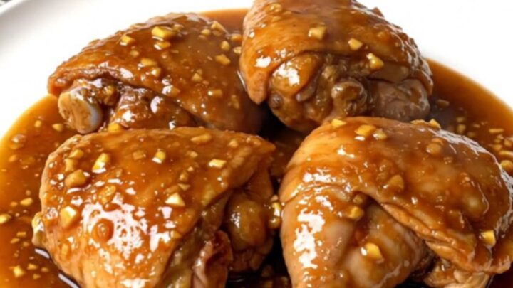 Close-up of slow-cooked brown sugar garlic chicken thighs in a black ceramic slow cooker with a serving spoon.