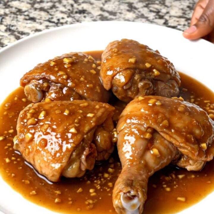 Close-up of slow-cooked brown sugar garlic chicken thighs in a black ceramic slow cooker with a serving spoon.