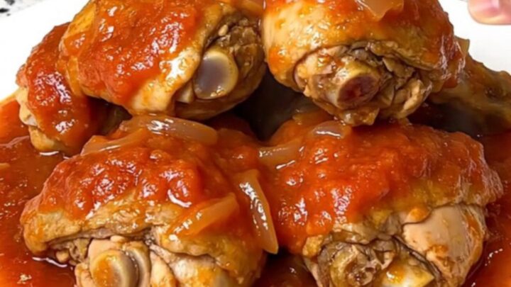 A top-down view of six bone-in chicken thighs simmering in a rich tomato gravy inside a black slow cooker.