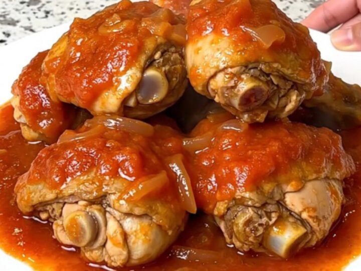 A top-down view of six bone-in chicken thighs simmering in a rich tomato gravy inside a black slow cooker.