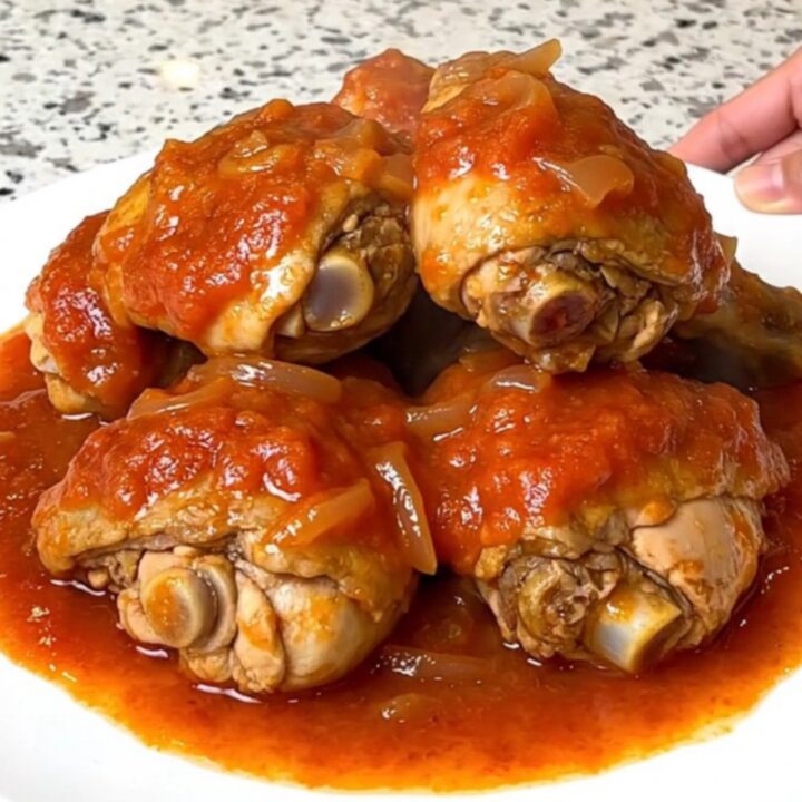 A top-down view of six bone-in chicken thighs simmering in a rich tomato gravy inside a black slow cooker.