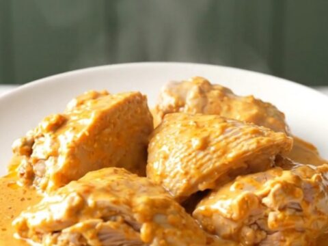A top-down view of cooked chicken thighs in a slow cooker, covered in a creamy