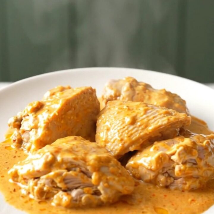 A top-down view of cooked chicken thighs in a slow cooker, covered in a creamy