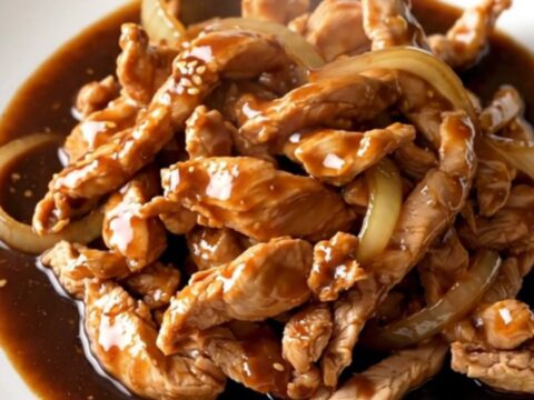 A close-up of tender, braised chicken thigh strips coated in a rich, dark bulgogi sauce with soft onions
