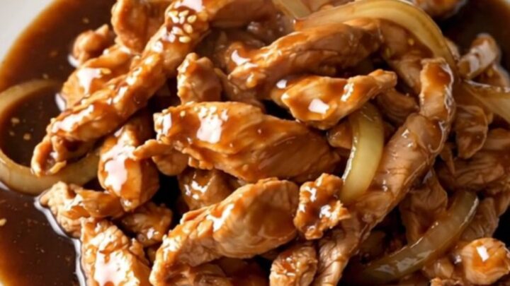 A close-up of tender, braised chicken thigh strips coated in a rich, dark bulgogi sauce with soft onions