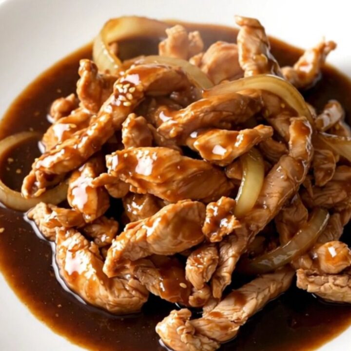 A close-up of tender, braised chicken thigh strips coated in a rich, dark bulgogi sauce with soft onions