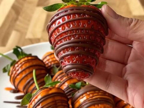 A close-up of pumpkin-shaped strawberries on a white plate with a blurred kitchen background.