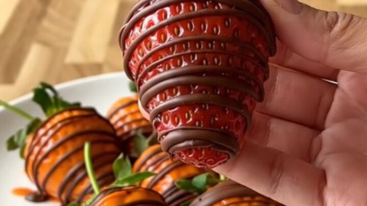 A close-up of pumpkin-shaped strawberries on a white plate with a blurred kitchen background.