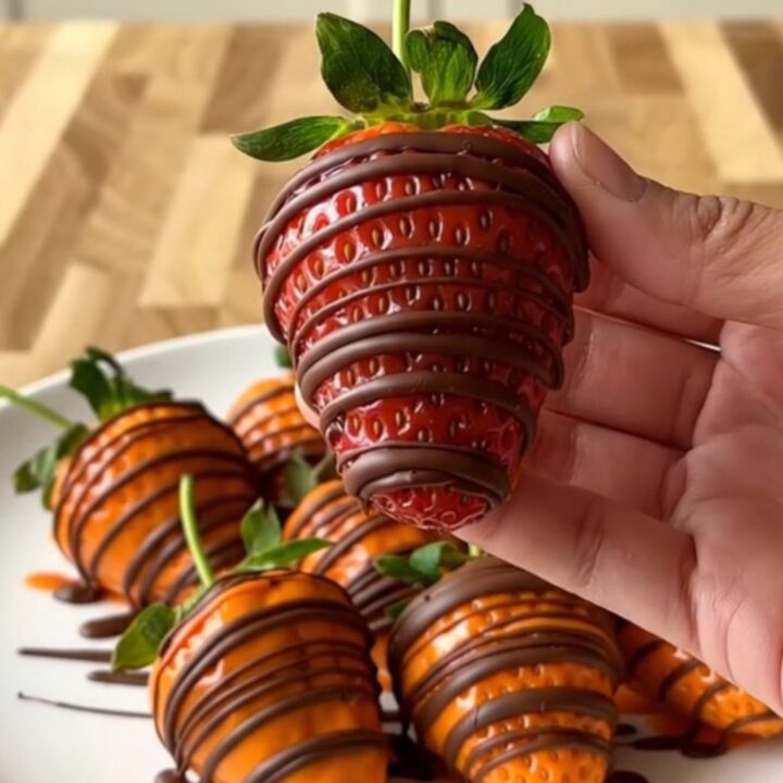 A close-up of pumpkin-shaped strawberries on a white plate with a blurred kitchen background.
