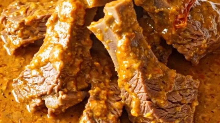 A close-up of tender beef chuck cubes in a rich, creamy sun-dried tomato sauce inside a slow cooker.