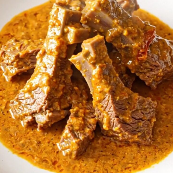 A close-up of tender beef chuck cubes in a rich, creamy sun-dried tomato sauce inside a slow cooker.