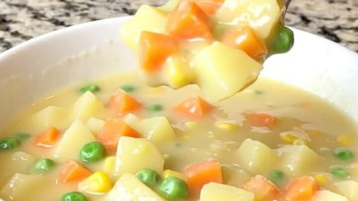 A top-down view into a slow cooker filled with a creamy, cheesy vegetable soup with potatoes and peas.