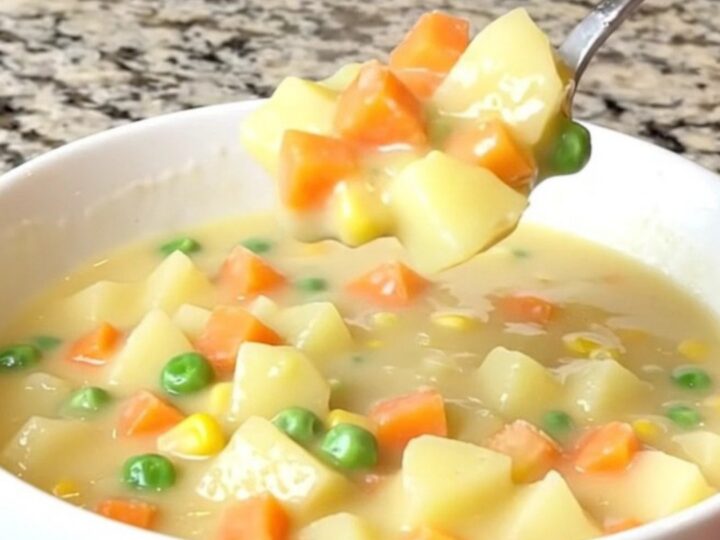 A top-down view into a slow cooker filled with a creamy, cheesy vegetable soup with potatoes and peas.