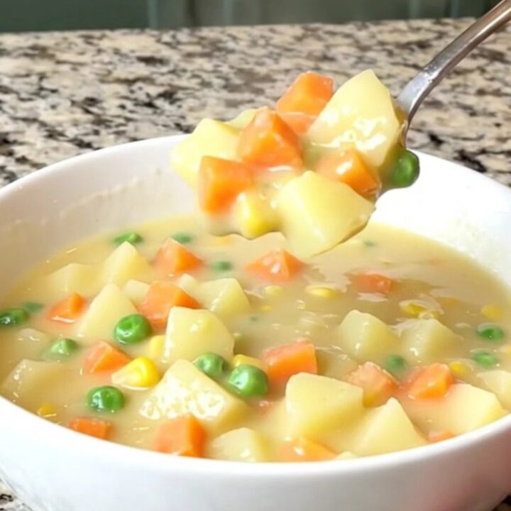 A top-down view into a slow cooker filled with a creamy, cheesy vegetable soup with potatoes and peas.