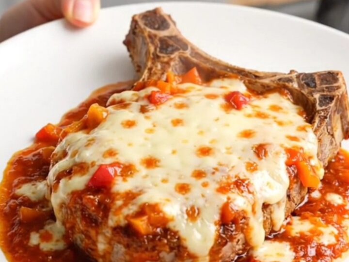 A stainless steel slow cooker filled with tender pork chops, peppers, onions, and melted mozzarella cheese.