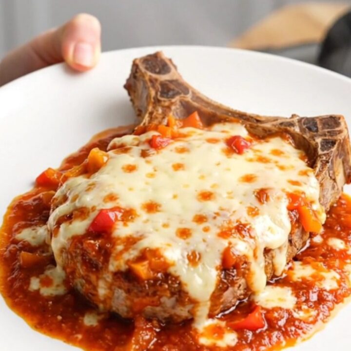 A stainless steel slow cooker filled with tender pork chops, peppers, onions, and melted mozzarella cheese.
