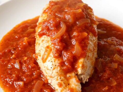 A close-up of tender chicken breast covered in a vibrant, spicy red tomato sauce with onions.