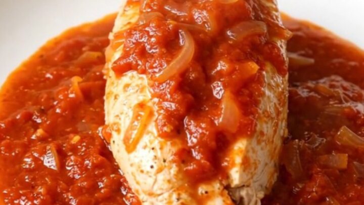 A close-up of tender chicken breast covered in a vibrant, spicy red tomato sauce with onions.