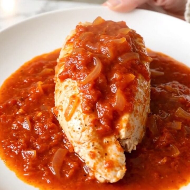A close-up of tender chicken breast covered in a vibrant, spicy red tomato sauce with onions.