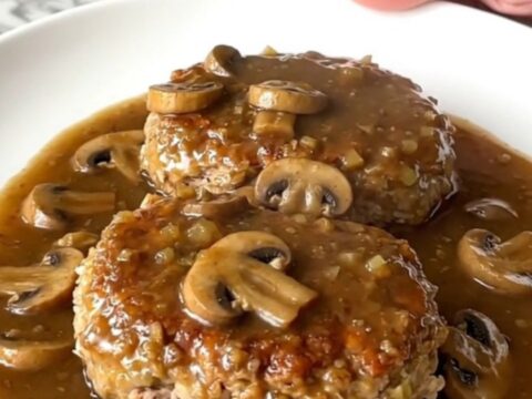 A serving spoon lifting a tender turkey Salisbury steak covered in rich mushroom gravy from a slow cooker.