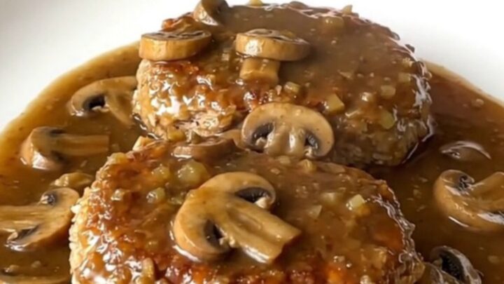 A serving spoon lifting a tender turkey Salisbury steak covered in rich mushroom gravy from a slow cooker.